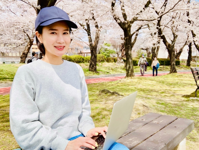 公園で桜のしたでPC作業する女性
